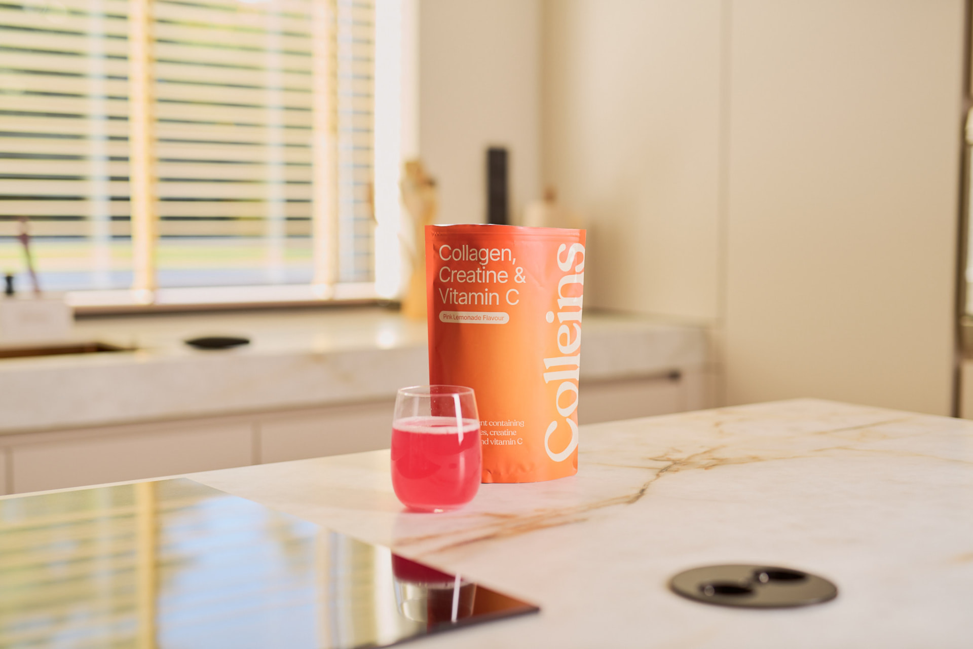Colleins Collagen, Creatine & Vitamine C op het aanrecht met een glas pink lemonade